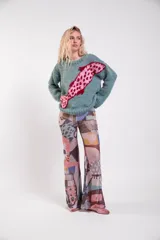 Sweater de lana merino tejido a mano, de color verde con diseño de ballena en intarsia de tonos rosados y rojos que cruza la prenda. Presenta cuello redondo, mangas largas y calce holgado.
