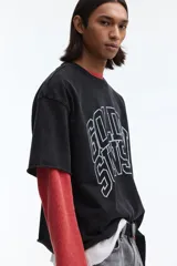 Remera boxy de algodón negro con efecto deslavado, corte oversized y mangas cortas. Presenta un estampado gráfico frontal con la inscripción "Golden Sunset" en estilo universitario.