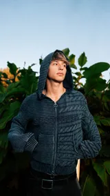 Campera de punto de doble textura y cierre frontal completo con capucha, de color gris oscuro, con bolsillos tipo canguro y el nombre de la marca bordado en el pecho.