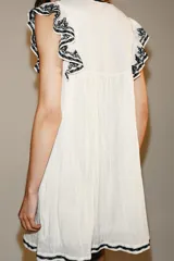 Vestido corto blanco de Zara Woman Collection con bordados en contraste de color negro, escote en V y mangas sisa con pequeños volados.