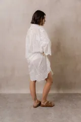 Camisola blanca de silueta amplia y caída liviana, con bordados florales sutiles, cuello camisero, cierre frontal de botones y mangas 3/4.