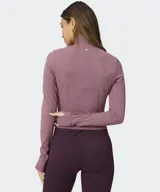 Campera Fabletics modelo Perfect Storm Cropped, de color rosado con cierre frontal completo, cuello alto, mangas largas con aberturas para pulgares y bolsillos laterales.