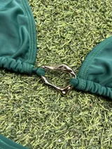 Conjunto de bikini verde con corpiño triangular con argolla metálica en el centro y bombacha colaless con tiras para atar y argollas en los costados.