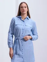 Vestido camisero corto a rayas verticales celestes y blancas, con cuello con solapa, abertura frontal con botones, dos bolsillos de parche en el pecho y lazo de ajuste en la cintura.