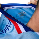 Camiseta de fútbol Umbro del Club Nacional de Football, tercera equipación modelo Away 3. Diseño en color celeste con cuello polo y puños en azul, blanco y rojo. Incluye logo de Umbro, escudo del club y el sponsor Antel en el frente.
