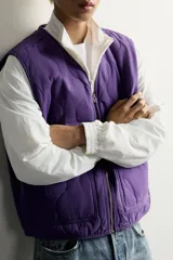 Chaleco acolchado de algodón color violeta con efecto lavado, cuello en V, cierre frontal con cremallera y bolsillos de plastrón delanteros.