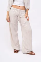 Pantalón largo de mujer, de corte amplio y tiro alto, con estampado a rayas verticales en tonos beige y blanco. Tiene cintura elástica con cordón ajustable.