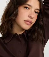 Blusa tipo polo de manga larga, confeccionada en tejido interlock de algodón y poliéster. Presenta cuello clásico con cierre frontal de botones y diseño básico liso.