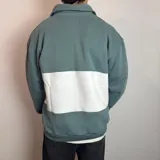 Buzo de algodón con medio cierre frontal y cuello tipo polo. Presenta un diseño de bloques de color en tonos gris oscuro y blanco, con bordados decorativos en el pecho.