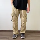 Pantalón cargo tipo parachute de color beige, con calce baggy, bolsillos laterales con solapa y cordones ajustables en los tobillos.