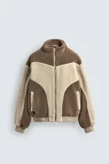 Cazadora de corte relajado confeccionada en tejido de borreguillo con diseño de paneles en tonos marrón y beige. Presenta cuello subido, cierre frontal de cremallera, bolsillos laterales y acabados en rib en puños y cintura.