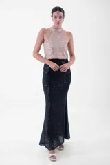 Vestido largo de fiesta con lentejuelas, compuesto por un top verde esmeralda con cuello halter y una falda negra ajustada con abertura lateral.