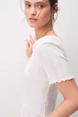 Remera de algodón blanca de manga corta, con diseño texturado, escote redondo y pequeño lazo decorativo en el centro. Presenta terminaciones con ondas en cuello, mangas y ruedo.