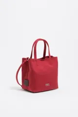 Bolso de mano pequeño tipo tote bag, color rojo, confeccionado en gabardina con detalles en piel. Posee asas de mano y correa ajustable para llevar al hombro o cruzado. Lleva placa metálica con el logo de la marca en el frente.