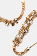 Pack de dos pulseras doradas con doble cordón metálico tipo malla, apliques decorativos de joyas a contraste y cierre corredizo con cuenta esférica.