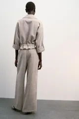 Chaqueta jaspeada color beige, con cuello solapa, manga tres cuartos con trabilla y botón, bolsillos delanteros de plastrón con solapa, bajo ajustable con cordones interiores y cierre frontal con botones a presión.