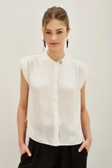 Camisa de corte oversize color negro, con cuello mao, mangas cortas y botones ocultos. Presenta un pin metálico decorativo con strass en el cuello.