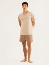 Pijama de hombre compuesto por una remera de manga corta y cuello redondo, color beige claro, con una costura horizontal decorativa en el pecho y un pequeño logo bordado. Se combina con un short de color marrón topo.