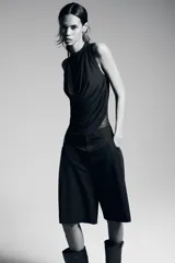 Body negro de tul con cuello alto y sisas amplias. Diseño drapeado en el frente y cierre inferior con broches a presión.