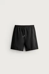 Bermuda estilo jogger de ajuste relajado, color negro, confeccionada en tejido interlock de algodón. Cuenta con cintura elástica ajustable mediante cordón, bolsillos delanteros tipo vivo y diseño liso.