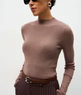 Suéter de punto canelado color beige, con cuello alto y manga larga. Presenta un diseño ajustado al cuerpo, confeccionado en una mezcla de viscosa, poliéster y poliamida.