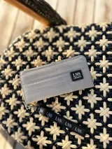 Billetera larga con cierre perimetral y diseño capitoneado. Cuenta con correa de mano desmontable con logo estampado y parche frontal con marca LNS. El interior incluye múltiples compartimentos para tarjetas y un bolsillo con cierre.