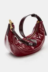 Bolso de hombro de diseño semicircular, confeccionado en material sintético efecto charol de color rojo. Cuenta con una correa ajustable fina con detalles metálicos dorados y cierre superior con cremallera.