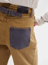 Pantalón jean de tiro alto y corte pinzado, con perneras de caída suelta y levemente anchas en el bajo. Posee pasador con hebilla en la parte trasera.