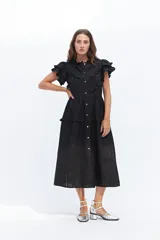 Vestido midi de lino blanco con diseño de broderie, cuello alto, cierre frontal con botones y volados decorativos en los hombros y el cuerpo.