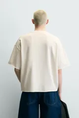 Sudadera boxy fit de color beige con interior de rizo, cuello redondo y manga corta. Presenta un estampado contrastante en el frente con la inscripción "Deep Founders London 90" y acabados irregulares en los bordes.