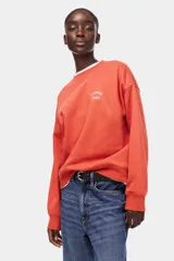 Buzo oversized de cuello redondo y manga larga, en color coral, con el texto 'L'AMOUR PARIS' bordado en el pecho en color blanco.