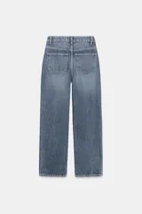 Jeans de mujer, tiro alto, color azul medio con efecto desgastado (lavado claro en muslos y oscuro en bordes). Corte recto y ancho (mom fit) con cinco bolsillos y cierre frontal de botón y cremallera.