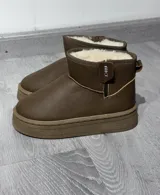 Botas tipo pantubota color marrón claro, con interior forrado en piel sintética blanca, suela de plataforma plana y cierre lateral.
