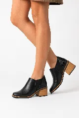 Botín de cuero color negro, de diseño minimalista con taco ancho símil madera, elásticos laterales y detalle texturado en el talón.