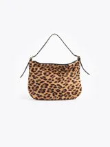 Cartera tipo hobo confeccionada en cuero con pelo vacuno estampado animal print. Presenta correa de hombro ajustable con detalles de hebillas metálicas en los laterales y cierre superior.