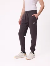 Babucha jogger color gris oscuro, con cintura elástica ajustable con cordón, bolsillos laterales y puños elásticos en los tobillos. Presenta un logo estampado en el muslo izquierdo.