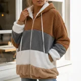 Campera peluda de mujer marca United Uy, con capucha y cierre frontal de cremallera. Presenta diseño de rayas horizontales en bloques de colores blanco, gris, beige y negro, con textura de piel sintética y puños elásticos.