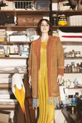 Tapado artesanal tejido en telar con lana teñida, presenta solapas y detalles en cuero natural. El diseño incluye terminaciones de flecos en el ruedo y una textura tejida en tonos naranja y ocre.