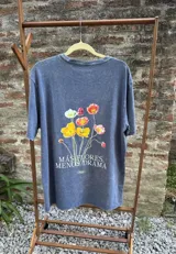 Remera blanca de manga corta, confeccionada en algodón premium, con estampa central de flores coloridas y la frase 'Más flores, menos drama'.