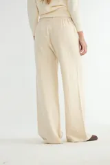 Pantalón de punto color crema, de corte recto y holgado, con cintura elástica y cordón ajustable. Presenta costuras verticales decorativas a lo largo de las piernas.