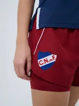 Short deportivo azul marino de mujer con calza interior celeste. Cuenta con cintura elástica ajustable con cordón y detalles de la marca Umbro y del Club Nacional de Football.
