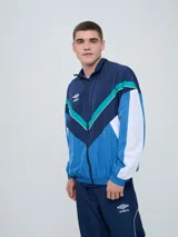 Campera de nailon Umbro modelo Beat, con cierre frontal completo y cuello alto. Diseño color block en tonos azul marino, azul brillante, celeste, blanco y verde menta, con cortes geométricos en el pecho y mangas largas.