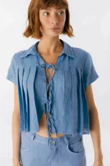 Blusa de lino color azul, de corte cropped y manga corta. Presenta cuello camisero, diseño con tablas frontales y cierre mediante lazos delgados en el centro.