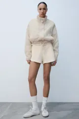 Chaqueta ligera de cuello subido y manga larga con estampado de lunares. Cuenta con bolsillos frontales de vivo, cierre de cremallera y botones a presión ocultos por solapa, y cordones ajustables en el bajo.