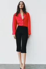 Camisa de popelina roja, de corte oversize, con cuello solapa, manga larga y bajo asimétrico redondeado. Cierre frontal oculto con botones.