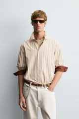 Camisa de corte relajado confeccionada en tejido con mezcla de viscosa, con diseño de rayas verticales en tonos beige y marrón. Presenta cuello solapa, cierre frontal de botones, manga larga con puños abotonados y un bolsillo en el pecho.