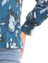 Blusa de seda fría con estampado floral en tonos verdes y azules. Presenta escote en V con un aplique metálico decorativo, mangas largas con puños y corte recto.