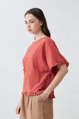 Blusa blanca de corte holgado con cuello redondo, mangas cortas con detalle de volados y ruedo con terminación de volado pequeño.