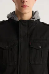 Campera militar negra con capucha gris de algodón, cierre frontal con cremallera y botones a presión, cuatro bolsillos frontales con solapa y charreteras en los hombros.
