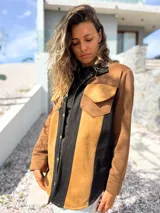 Sobre camisa de gamuza con diseño de paneles verticales en colores marrón, tostado y negro. Presenta cuello clásico, cierre frontal con botones metálicos y un bolsillo en el pecho con solapa.